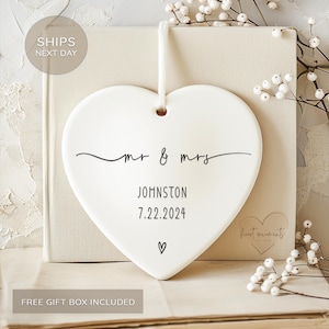 May include: White ceramic heart ornament with black calligraphy that reads "mr & mrs Johnston 7.22.2024" and a small heart symbol.