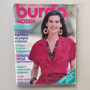 Puede incluir: Una portada de revista con una mujer que lleva una chaqueta rosa sobre una blusa estampada. La revista se titula "Burda Moden" y tiene el texto "Idealna tochnost vykroek" (Precisión ideal de los patrones) y "Cocktail iz uzorov i krasok" (Cóctel de patrones y colores).