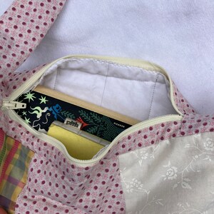 K&ouml;nnte beinhalten: Eine Patchwork-Stofftasche mit einem rosa-wei&szlig;en Blumenmuster. Die Tasche ist offen und enth&auml;lt ein Buch mit dem Text "PICADOR" auf dem Cover.