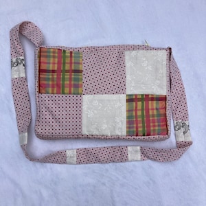 K&ouml;nnte beinhalten: Eine rosafarbene Patchwork-Stofftasche mit wei&szlig;em Punktmuster. Die Tasche hat einen langen Riemen und ist aus verschiedenen Stoffen mit Blumen- und Karomustern gefertigt.