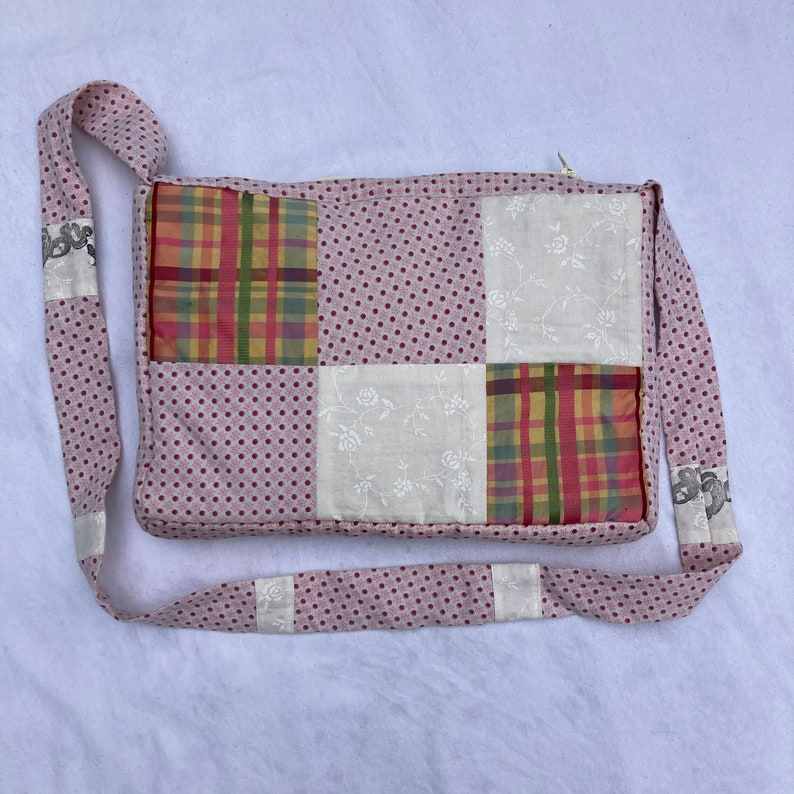 K&ouml;nnte beinhalten: Eine rosafarbene Patchwork-Stofftasche mit wei&szlig;em Punktmuster. Die Tasche hat einen langen Riemen und ist aus verschiedenen Stoffen mit Blumen- und Karomustern gefertigt.