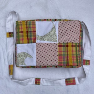 以下が含まれることがあります： 白いパッチワークのバッグで、長い白いストラップが付いています。バッグは、黄、赤、緑の色合いの格子柄、水玉模様、花柄など、さまざまな生地で作られています。