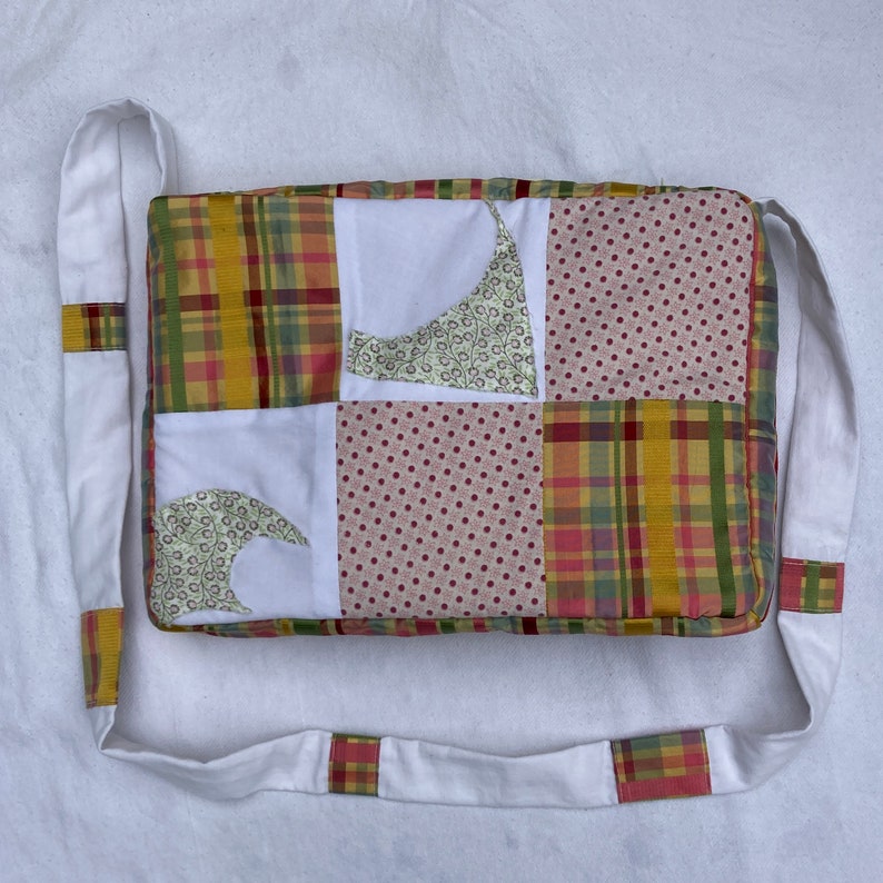 Może przedstawiać: Biała torba patchworkowa z długim białym paskiem. Torba jest wykonana z r&oacute;żnych tkanin, w tym kraty, groch&oacute;w i wzor&oacute;w kwiatowych w odcieniach ż&oacute;łtego, czerwonego i zielonego.