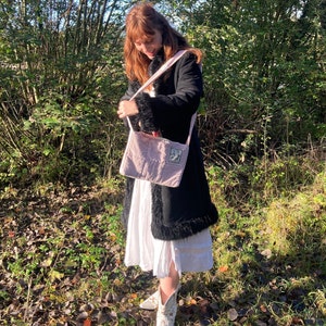 K&ouml;nnte beinhalten: Eine Frau tr&auml;gt einen schwarzen Mantel mit wei&szlig;em Pelzbesatz, ein wei&szlig;es Kleid und wei&szlig;e Cowboy-Stiefel. Sie tr&auml;gt eine rosafarbene gesteppte Tragetasche mit einem wei&szlig;en Riemen.