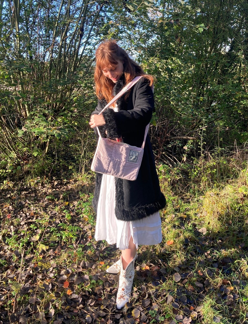 K&ouml;nnte beinhalten: Eine Frau tr&auml;gt einen schwarzen Mantel mit wei&szlig;em Pelzbesatz, ein wei&szlig;es Kleid und wei&szlig;e Cowboy-Stiefel. Sie tr&auml;gt eine rosafarbene gesteppte Tragetasche mit einem wei&szlig;en Riemen.