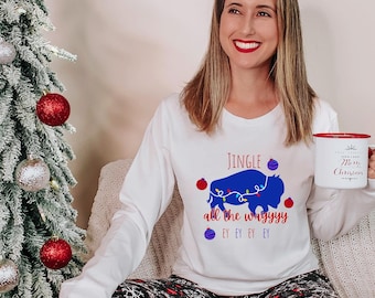 May include: White long-sleeve shirt with a blue buffalo graphic and the text "Jingle all the wayyyy". The shirt is paired with black and white snowflake patterned pajama pants. A white mug with red trim reads "Merry Christmas".