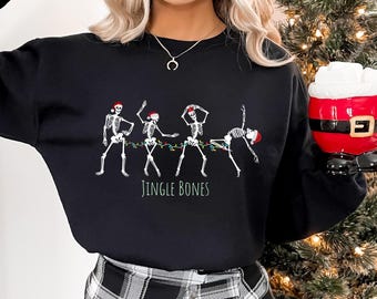 May include: Black sweatshirt with a graphic of five skeletons wearing Santa hats and holding Christmas lights. The text "Jingle Bones" is printed below the skeletons.