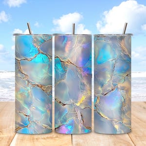 May include: Three stainless steel tumblers with lids and straws. The tumblers feature a shimmering, iridescent design with shades of blue, silver, and gold. The design resembles a geode or abstract marble pattern. The tumblers are cylindrical and appear to be approximately 8 inches tall.