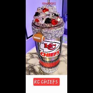 K&ouml;nnte beinhalten: Ein Edelstahlbecher mit einem rot-wei&szlig;-schwarzen Kansas City Chiefs Logo. Der Becher ist mit Strasssteinen verziert und hat einen roten Strohhalm. Der Becher ist mit Eis gef&uuml;llt und hat einen Fu&szlig;ball-Anh&auml;nger. Der Text "KC CHIEFS" ist unten im Bild gedruckt.