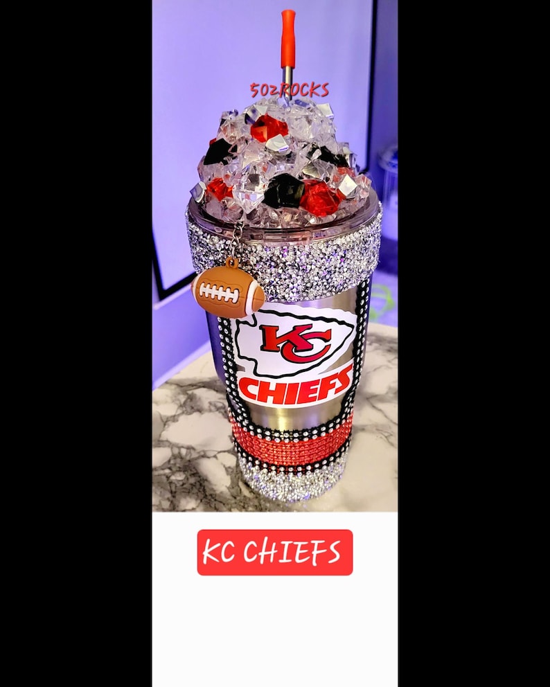 K&ouml;nnte beinhalten: Ein Edelstahlbecher mit einem rot-wei&szlig;-schwarzen Kansas City Chiefs Logo. Der Becher ist mit Strasssteinen verziert und hat einen roten Strohhalm. Der Becher ist mit Eis gef&uuml;llt und hat einen Fu&szlig;ball-Anh&auml;nger. Der Text "KC CHIEFS" ist unten im Bild gedruckt.