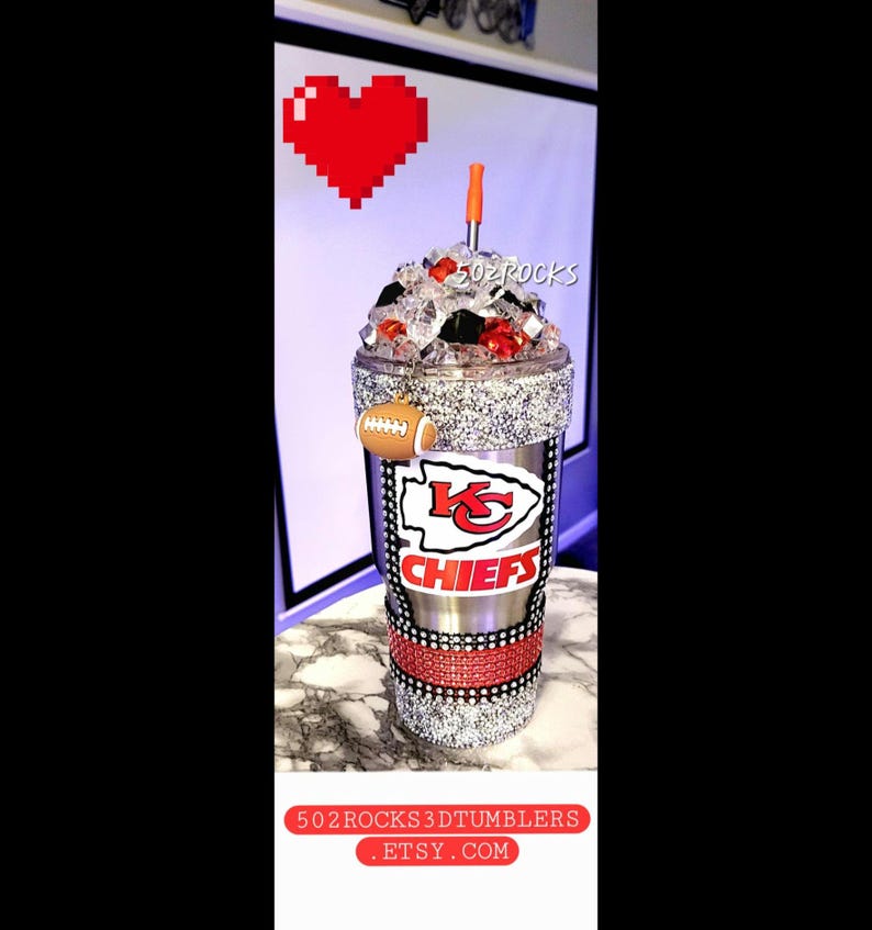 K&ouml;nnte beinhalten: Ein silberner und roter Kansas City Chiefs Becher mit Strasssteinen und einem Fu&szlig;ball-Anh&auml;nger. Der Becher ist mit Eis gef&uuml;llt und hat einen roten und schwarzen Strohhalm.