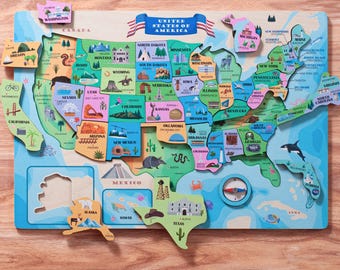 Puede incluir: Un rompecabezas de madera colorido de los Estados Unidos de América. Cada estado es una pieza separada con una ilustración y un nombre únicos. El rompecabezas está sobre un fondo azul con una brújula y una ballena.