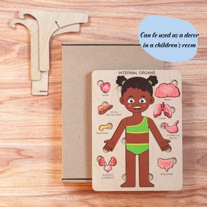Op de afbeelding: Houten puzzel met het lichaam van een kind met gelabelde interne organen. De puzzel bevat hart, hersenen, longen en andere organen. De tekst "INTERNAL ORGANS" staat bovenaan. De tekst "Can be used as a decor in a children's room" is ook aanwezig.