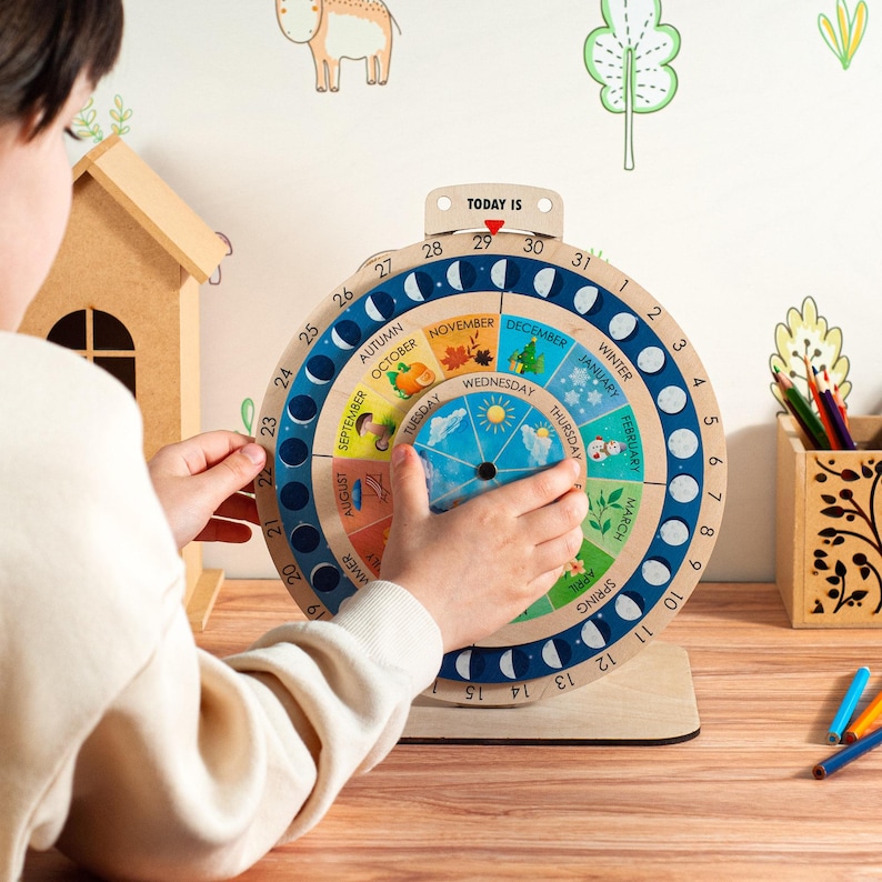 May include: A wooden perpetual calendar with a rotating wheel showing months, days, and phases of the moon. The calendar has a light wood base and a blue and white outer ring. The text "TODAY IS" is at the top.