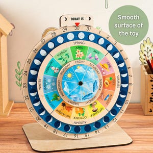 May include: Wooden educational calendar with a rotating wheel displaying months, days, and seasons. The calendar features colorful illustrations for each month and season, with a "Today Is" indicator. The base is made of light-colored wood.