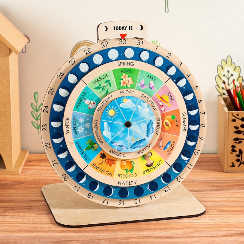 May include: Wooden educational calendar with a circular design. The calendar features months, days, and phases of the moon. The text "TODAY IS" is at the top. The calendar is on a wooden stand and is designed for educational purposes.