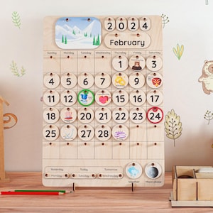 May include: Wooden perpetual calendar for February 2024, featuring a mountain scene and various holiday icons. Includes circular date markers and weather/moon phase indicators. The calendar is made of light-colored wood.