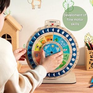 May include: Wooden educational calendar toy with a rotating wheel displaying months, days, and seasons. The calendar features colorful illustrations and the text "Development of fine motor skills". The toy is designed for children.