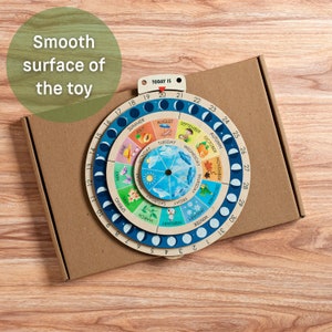 May include: A wooden educational toy depicting the phases of the moon, seasons, and days of the week. The circular design features colorful illustrations and the text "TODAY IS". The toy is packaged in a cardboard box.