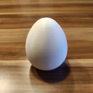 Puede incluir: Un objeto blanco, liso, con forma de huevo sobre una superficie de madera.