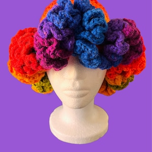 Op de afbeelding: Een kleurrijke gehaakte hoed met een regenboog van kleuren, waaronder rood, oranje, geel, groen, blauw, paars en roze. De hoed is gemaakt van garen en heeft een bloemenontwerp.
