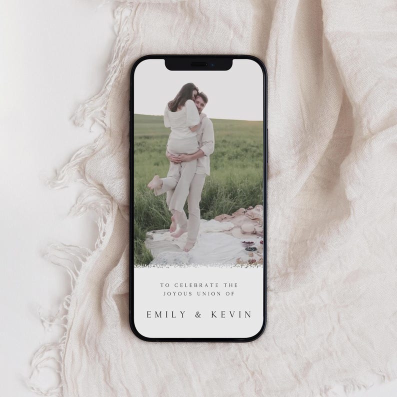 May include: A mobile phone screen displaying a wedding announcement with a photo of a couple in a field. The text reads "To celebrate the joyous union of Emily & Kevin".