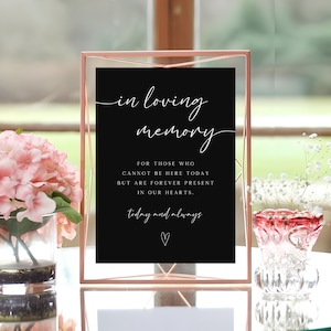May include: A black sign with a gold frame reads "in loving memory" and "For those who cannot be here today but are forever present in our hearts. today and always" with a small heart symbol.