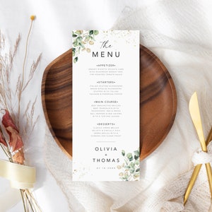 May include: A wedding menu card with a gold and white background and green foliage. The menu includes appetizers, starters, main course, and desserts. The names Olivia and Thomas are at the bottom of the card with the date 07.10.20XX.