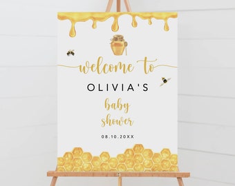 May include: White welcome sign with gold dripping honey, honeycomb, and bees. The sign reads "Welcome to Olivia's Baby Shower 08.10.20XX".