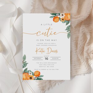 Puede incluir: Una invitaci&oacute;n de baby shower blanca con ilustraciones florales de color naranja y verde. El texto dice "A Little Cutie Is On The Way" e incluye el nombre "Katie Davis" y la fecha y hora del evento.