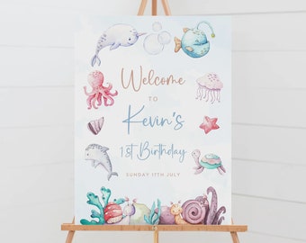 May include: A blue and white welcome sign with watercolour illustrations of sea creatures, including a narwhal, octopus, jellyfish, dolphin, turtle, and snail. The sign reads "Welcome to Kevin's 1st Birthday, Sunday 17th July".