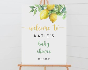 May include: Welcome to Katie's baby shower sign with a watercolor illustration of lemons and green leaves. The text is in gold and green on a white background. The date of the shower is 08.10.20XX.