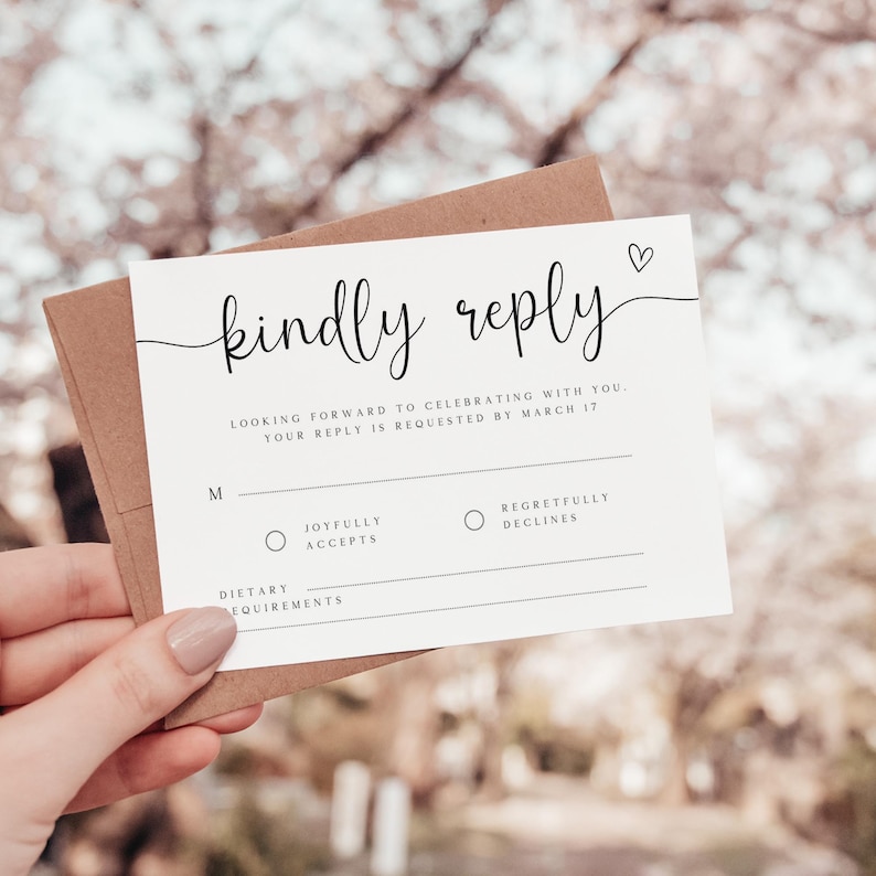 May include: A white RSVP card with black text that reads "kindly reply". The card has a small heart symbol in the top right corner. The text below reads "Looking forward to celebrating with you. Your reply is requested by March 17". There are two radio buttons with the text "Joyfully accepts" and "Regretfully declines". There is a line for dietary requirements.