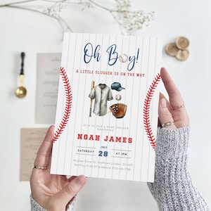 May include: A white and blue baseball-themed baby shower invitation with red stitching. The invitation says "Oh Boy! A Little Slugger Is On The Way" and includes the name "Noah James" and the date "July 28".