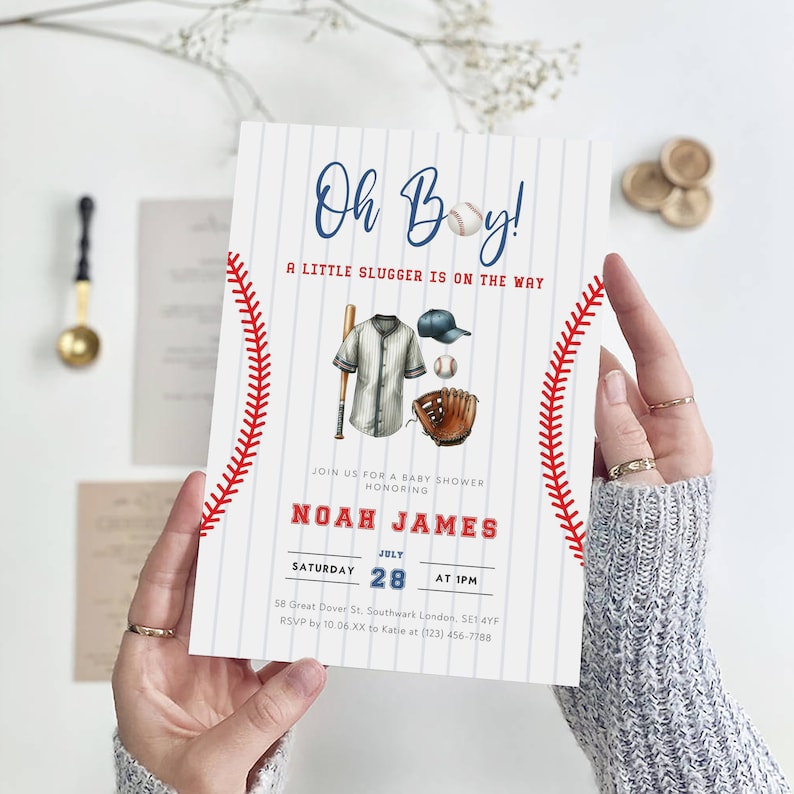 May include: A white and blue baseball-themed baby shower invitation with red stitching. The invitation says "Oh Boy! A Little Slugger Is On The Way" and includes the name "Noah James" and the date "July 28".