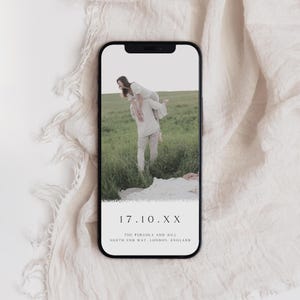 May include: A mobile phone screen displaying a wedding save the date announcement. The image shows a couple in a field, with the text "17.10.XX THE PERGOLA AND HILL NORTH END WAY, LONDON, ENGLAND" on the screen.