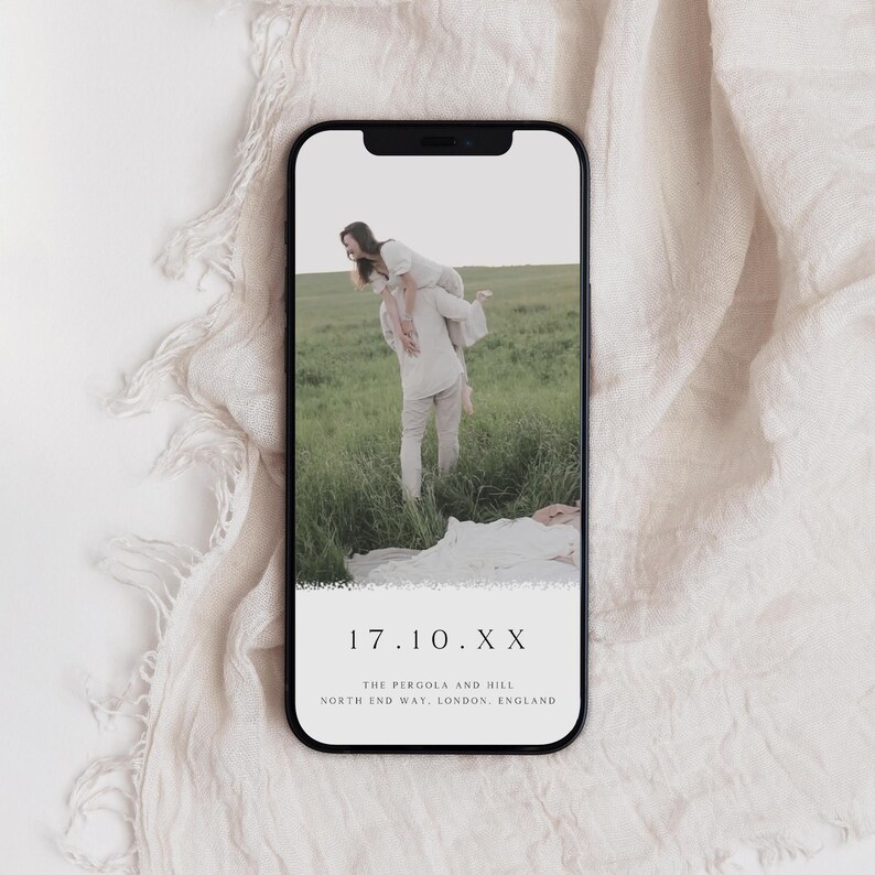 May include: A mobile phone screen displaying a wedding save the date announcement. The image shows a couple in a field, with the text "17.10.XX THE PERGOLA AND HILL NORTH END WAY, LONDON, ENGLAND" on the screen.