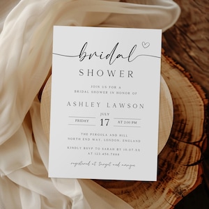 Puede incluir: Una tarjeta de invitaci&oacute;n blanca con las palabras "bridal shower" en escritura elegante. La tarjeta incluye detalles para la despedida de soltera de Ashley Lawson, incluyendo la fecha, hora y lugar en Londres, Inglaterra.