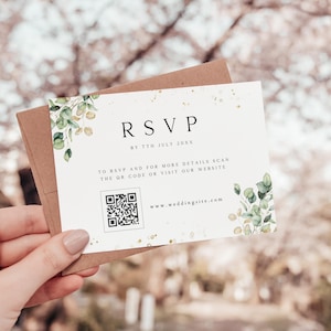Puede incluir: Tarjeta RSVP blanca con purpurina dorada y follaje verde. La tarjeta incluye el texto "RSVP antes del 7 de julio de 20XX" y un código QR con el texto "Para RSVP y para más detalles escanea el código QR o visita nuestro sitio web www.weddingsite.com"