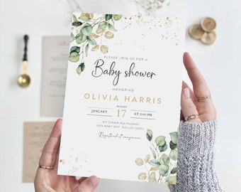 May include: A white baby shower invitation with gold lettering and a watercolor illustration of green leaves. The invitation reads "Please join us for a Baby Shower honoring Olivia Harris, August 17 at 2:00 PM, Ida Claria Restaurant, 3456 Baby Way, Dallas, Texas. Registered at anagomaom."