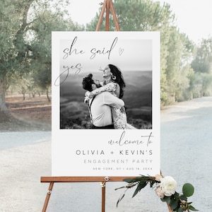Puede incluir: Una foto en blanco y negro de una pareja abrazándose, con el texto "she said yes" y un pequeño corazón encima. Debajo de la foto, dice "welcome to Olivia + Kevin's Engagement Party" y la fecha y la ubicación de la fiesta.