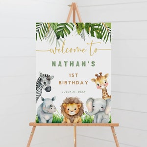 May include: Welcome to Nathan's 1st Birthday sign with a jungle theme. The sign features a zebra, giraffe, rhino, and elephant with green leaves and gold lettering.
