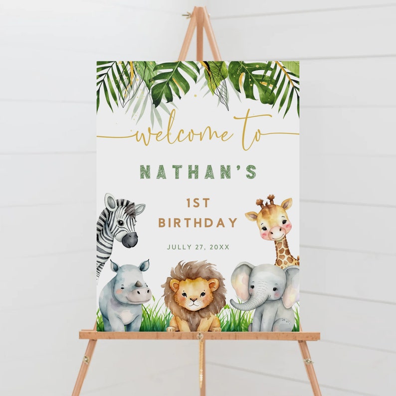 May include: Welcome to Nathan's 1st Birthday sign with a jungle theme. The sign features a zebra, giraffe, rhino, and elephant with green leaves and gold lettering.