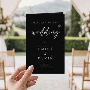 Può includere: Un cartello di benvenuto per matrimoni nero con testo bianco, tenuto in mano. Il cartello recita "WELCOME TO THE wedding OF EMILY & KEVIN". La data e il luogo sono in basso.
