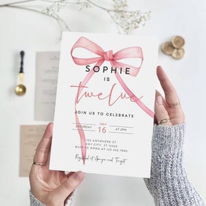 K&ouml;nnte beinhalten: Ein rosa Aquarell-Schleife mit dem Text "Sophie ist zw&ouml;lf" auf wei&szlig;em Hintergrund. Die Einladung enth&auml;lt Details f&uuml;r eine Geburtstagsfeier am 16. Juli um 14:00 Uhr. Die Adresse und RSVP-Informationen sind ebenfalls enthalten. Die Einladung gibt an, dass die Veranstaltung bei Amazon und Target registriert ist.