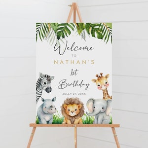 Op de afbeelding: Welkom bij Nathans 1e verjaardagsschild met een jungle thema. Het bord toont een zebra, een giraffe, een neushoorn, een leeuw en een olifant met groene bladeren en gouden glitter. De datum is 27 juli 20XX.