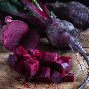 May include: A close-up of a wooden cutting board with a whole beet, a beet cut in half, and diced beets. The beets are a deep, vibrant purple color.