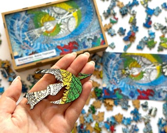 May include: A wooden jigsaw puzzle featuring a colorful bird design. The puzzle pieces are scattered around a wooden box and a completed image. The bird has white, green, yellow, and blue details. The box has text on it.