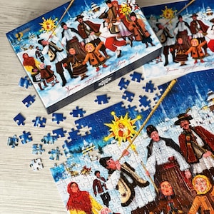 May include: A 500-piece jigsaw puzzle with a winter scene featuring people in traditional clothing. The box and assembled puzzle show a festive illustration with a sun and text. Scattered puzzle pieces are visible.
