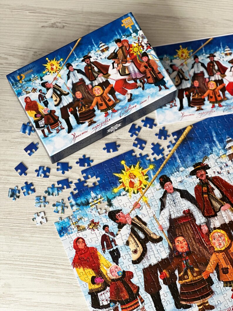 May include: A 500-piece jigsaw puzzle with a winter scene featuring people in traditional clothing. The box and assembled puzzle show a festive illustration with a sun and text. Scattered puzzle pieces are visible.